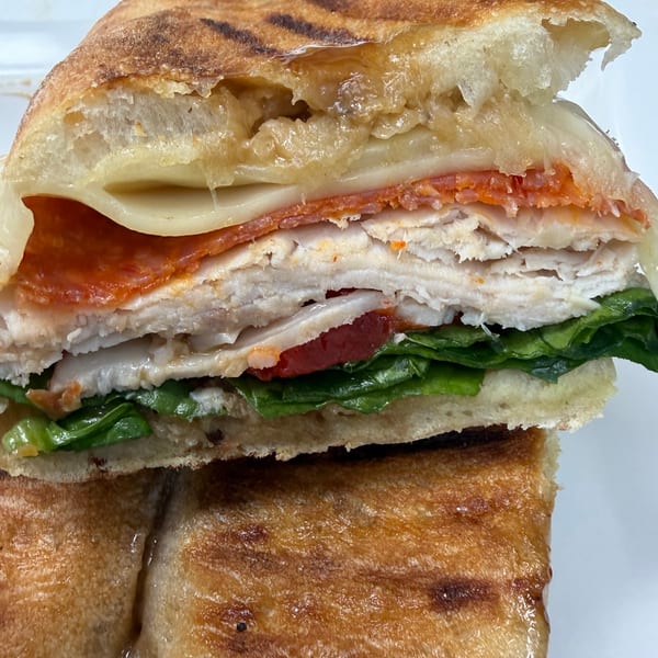Close-up of a panini sandwich, revealing layers of turkey, pepperoni, melted cheese, and fresh greens.