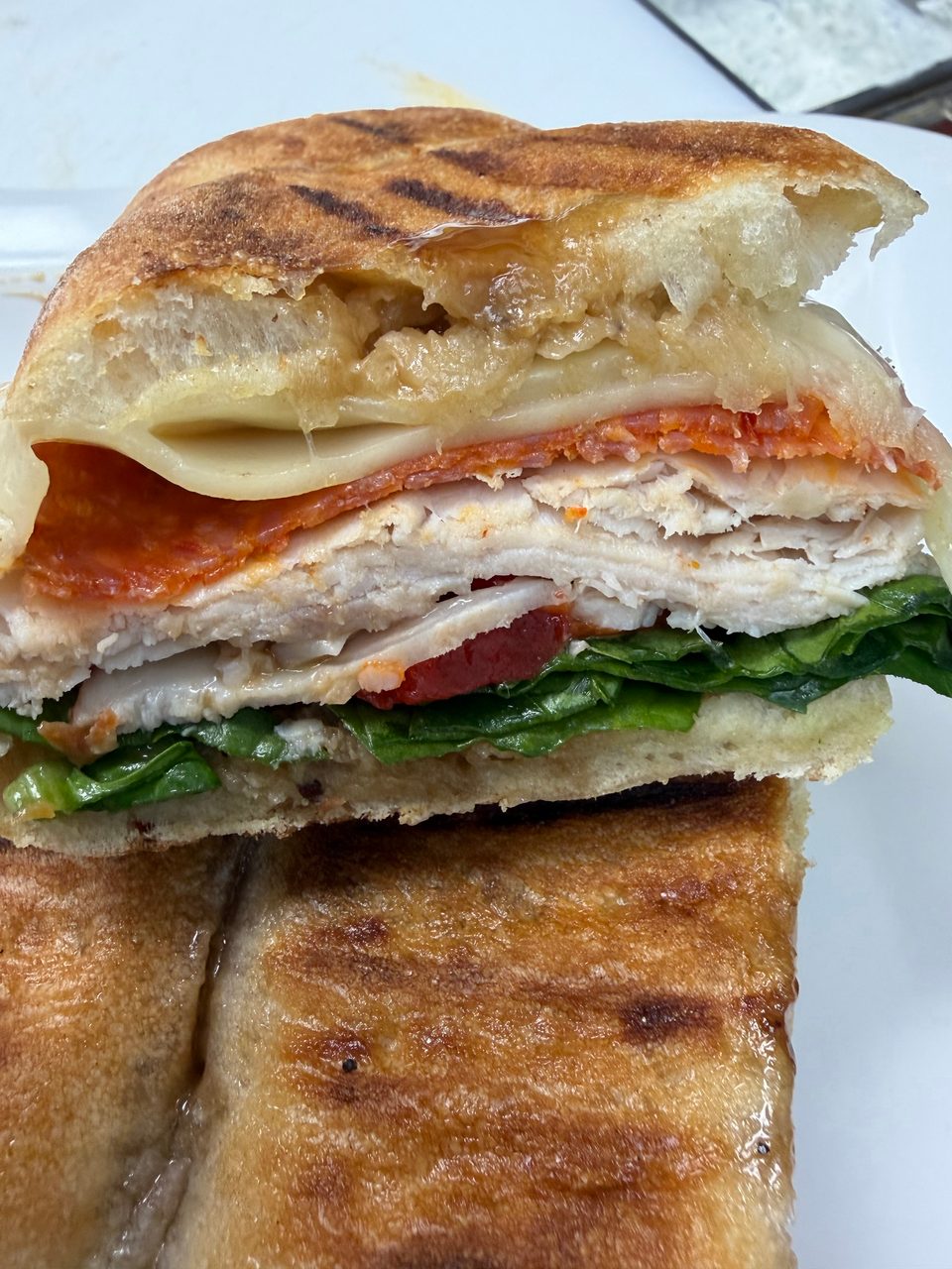 Close-up of a panini sandwich, revealing layers of turkey, pepperoni, melted cheese, and fresh greens.