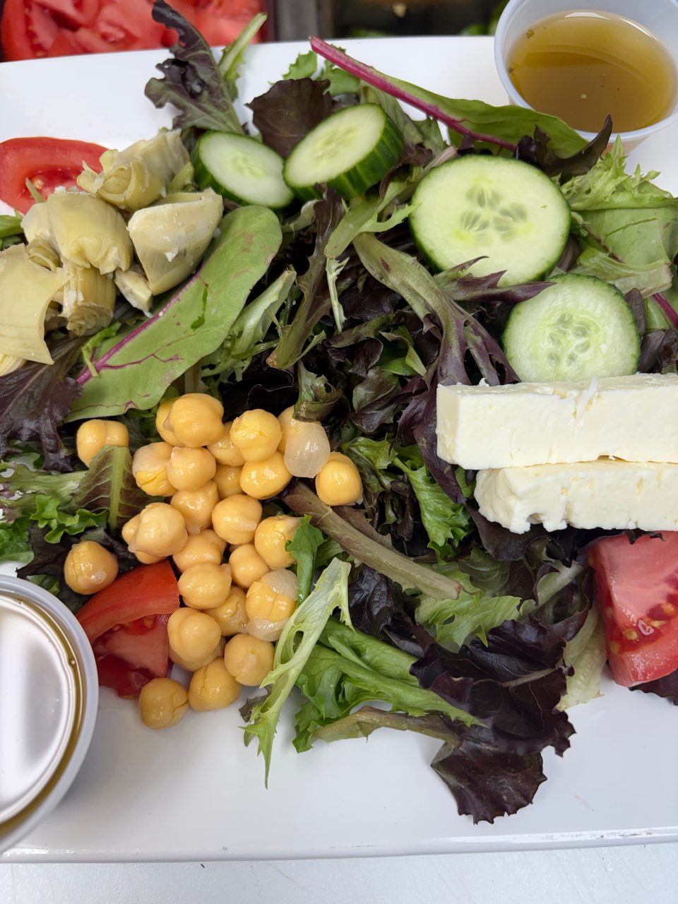 Close-up of a fresh garden salad with chickpeas, artichoke hearts, cucumbers, tomatoes, and feta cheese.