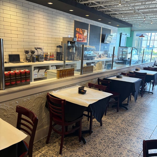 Interior of a cafe with tables and chairs, a coffee bar, and patterned floor tiles.