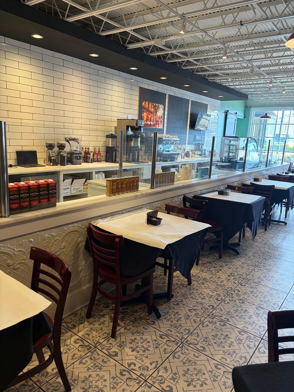 Interior of a cafe with tables and chairs, a coffee bar, and patterned floor tiles.
