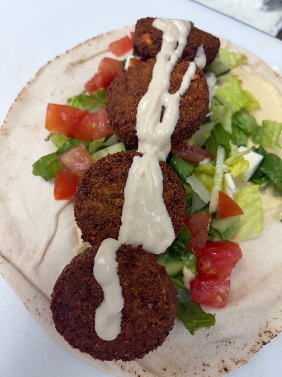 Four falafel balls drizzled with tahini sauce, served on pita bread with lettuce and diced tomatoes.