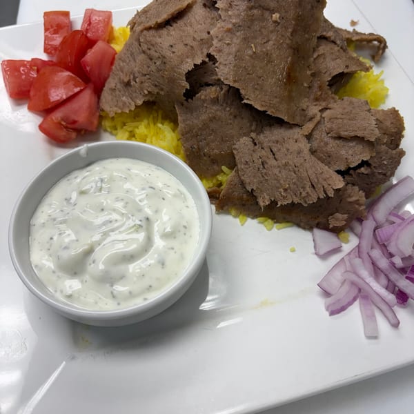 Gyro meat and yellow rice with a side of diced tomatoes, tzatziki sauce, and sliced red onions.