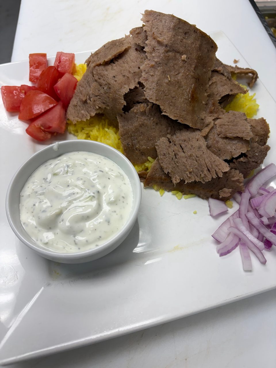 Gyro meat and yellow rice with a side of diced tomatoes, tzatziki sauce, and sliced red onions.