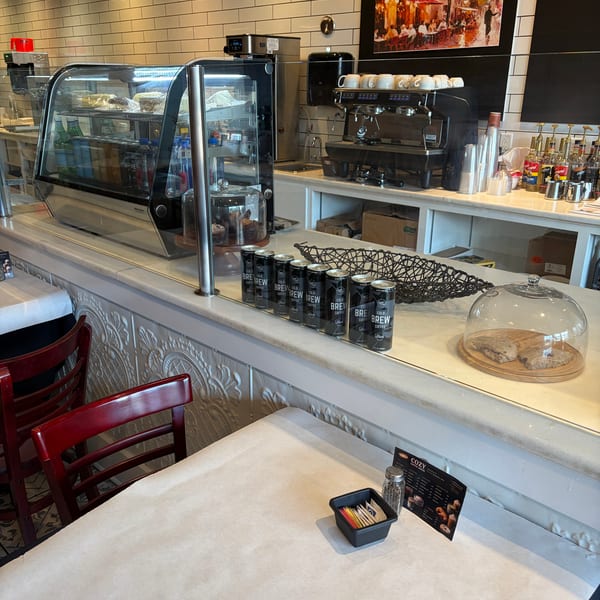 A cafe interior with a pastry display, coffee machine, cold brew cans, and a table with a menu.