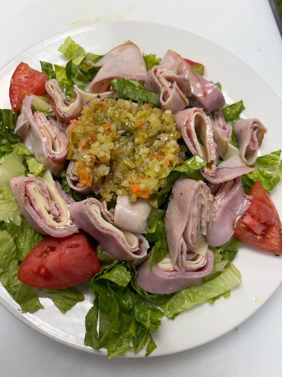 Ham and cheese roll-ups with relish and tomato wedges on a bed of lettuce.