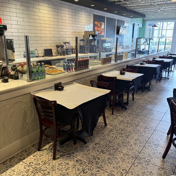 A modern cafe interior with a long counter, display cases, and dining tables with dark tablecloths.