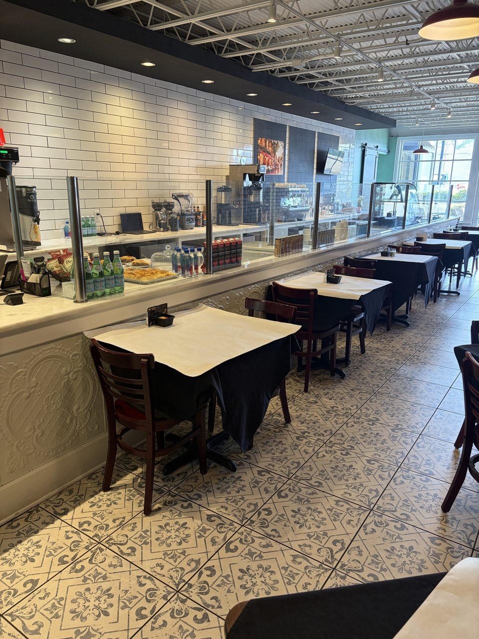 A modern cafe interior with a long counter, display cases, and dining tables with dark tablecloths.
