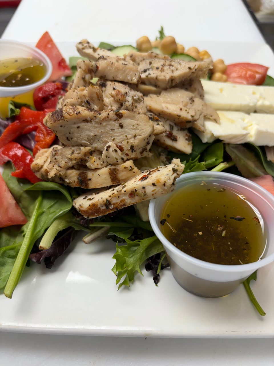 Grilled chicken salad with feta, chickpeas, tomatoes, peppers, and two cups of dressing.