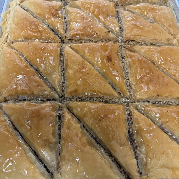 Close-up of a tray of golden-brown baklava pastries, cut into triangles and drizzled with syrup.