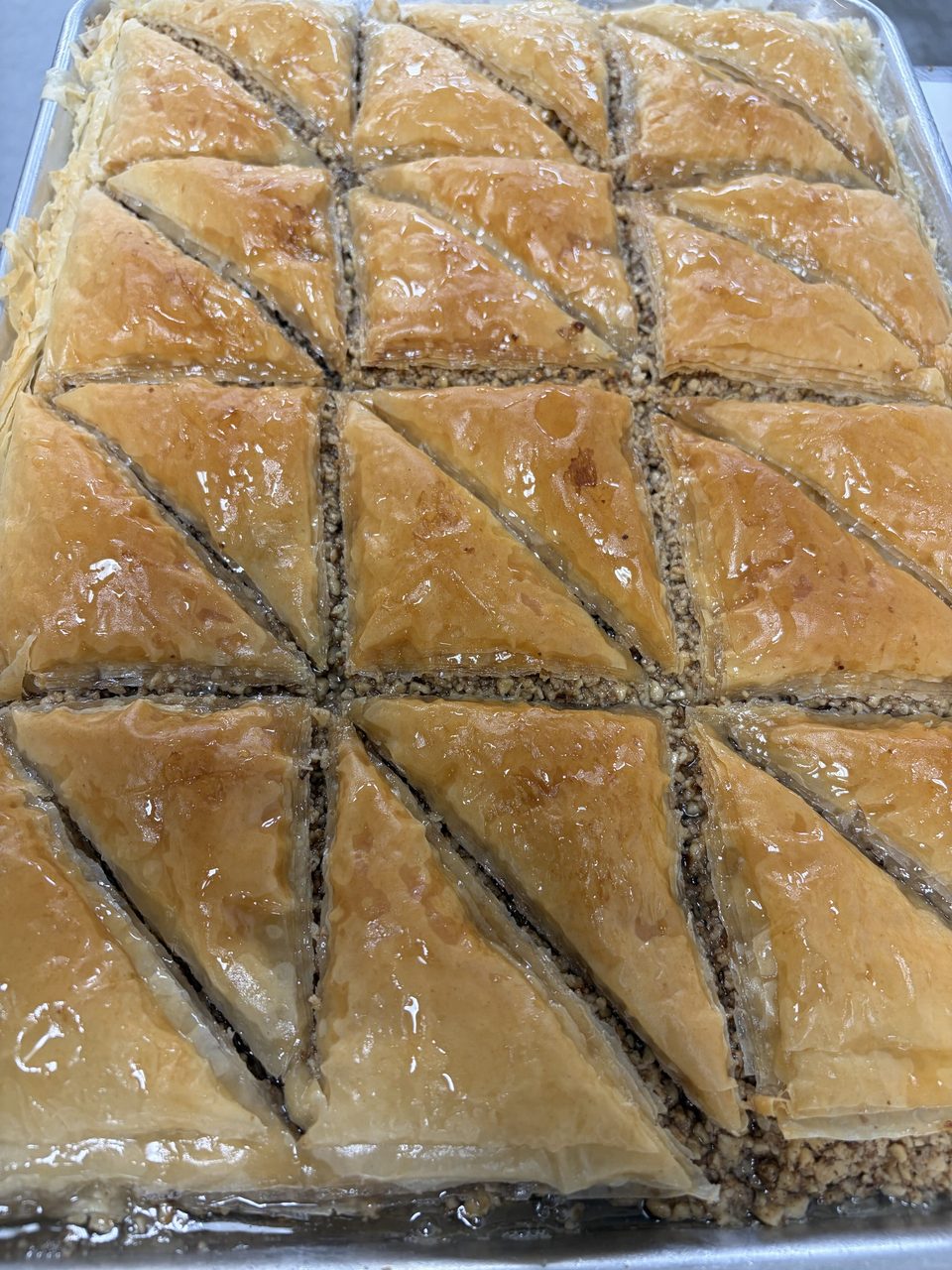 Close-up of a tray of golden-brown baklava pastries, cut into triangles and drizzled with syrup.