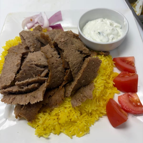 Gyro meat slices over yellow rice with red onion, tomato wedges, and tzatziki sauce.