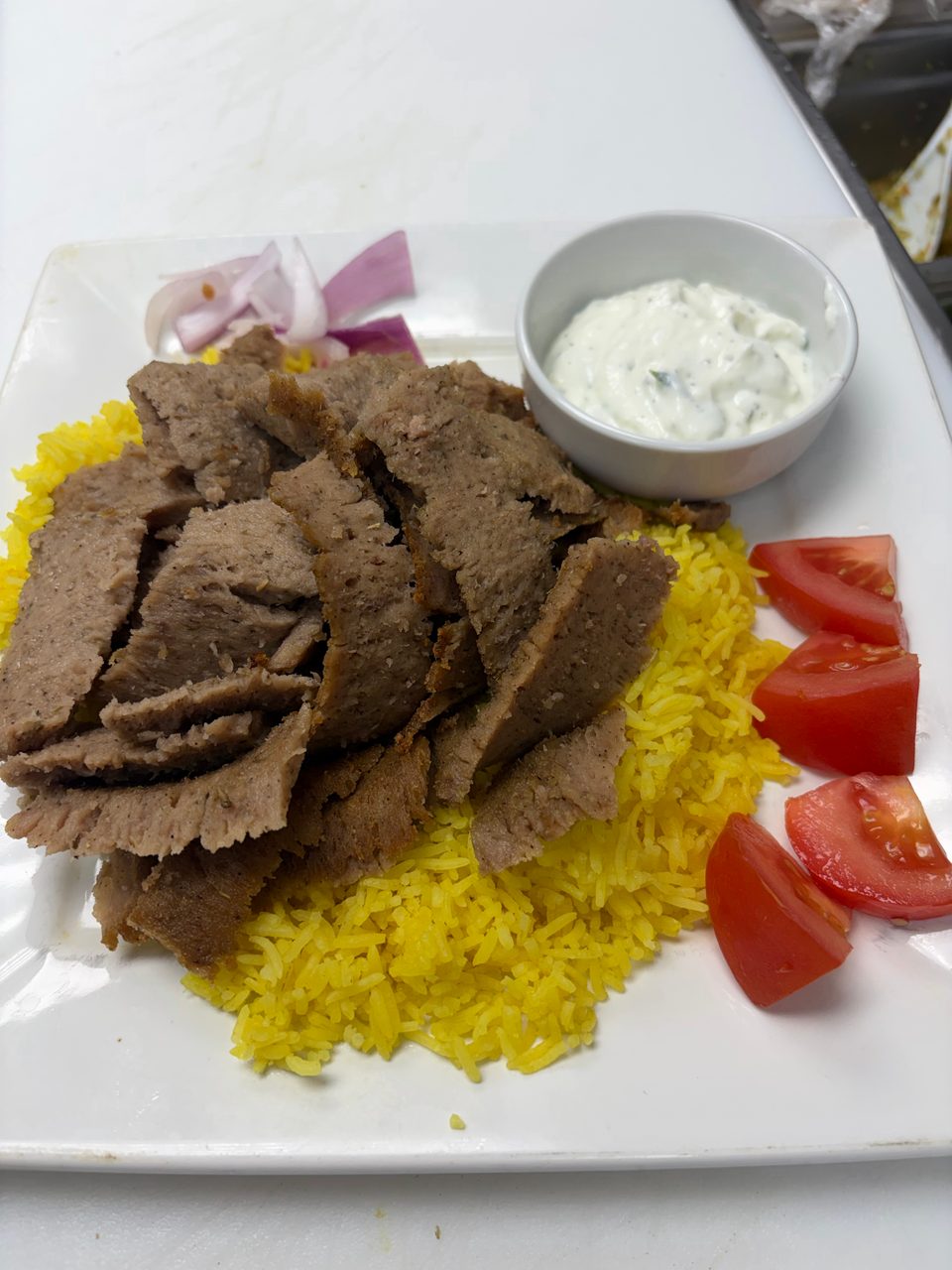 Gyro meat slices over yellow rice with red onion, tomato wedges, and tzatziki sauce.