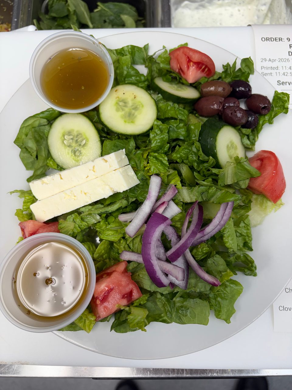 A fresh Greek salad with lettuce, cucumbers, tomatoes, olives, feta cheese, and red onions.