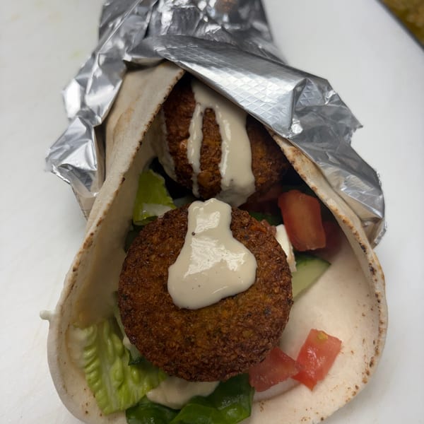 Falafel wrap with lettuce, tomatoes, cucumbers, and tahini sauce, partially wrapped in foil.