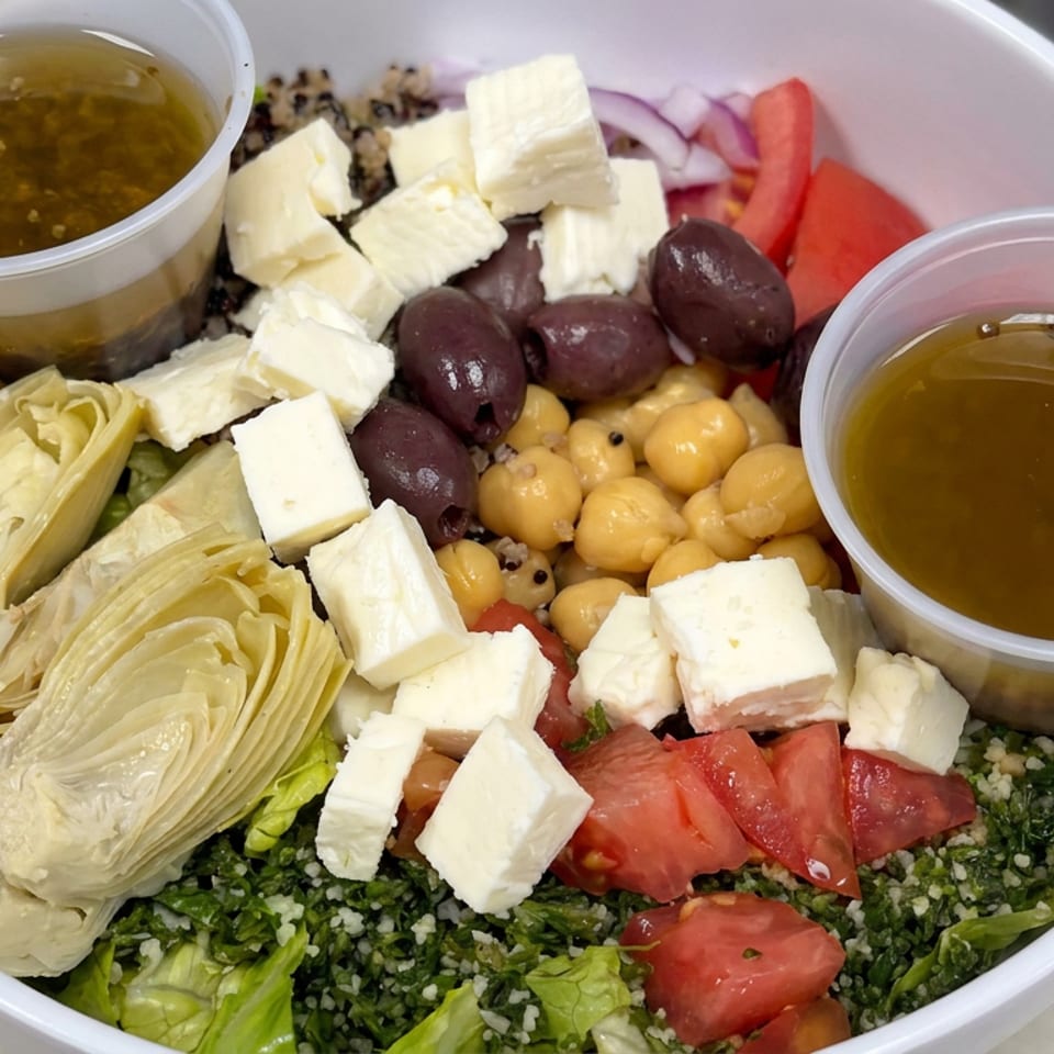 Mediterranean salad bowl with feta, chickpeas, olives, artichokes, tomatoes, tabbouleh, and two cups of dressing.