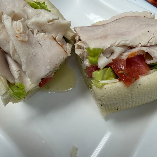 A turkey sub sandwich, cut in half, with lettuce, tomatoes, and dressing on a white plate.
