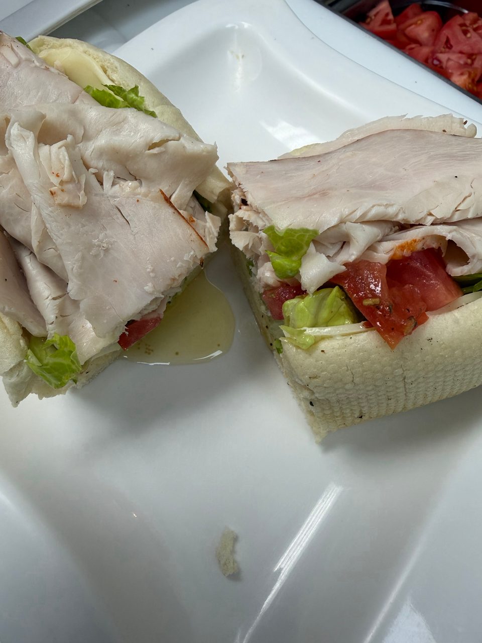 A turkey sub sandwich, cut in half, with lettuce, tomatoes, and dressing on a white plate.