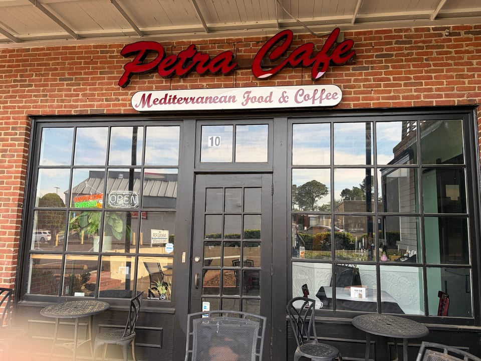 Exterior of Petra Cafe, a Mediterranean restaurant, with outdoor seating and an "Open" sign.