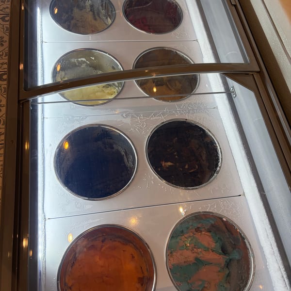 A freezer display case with eight round containers of various ice cream flavors.