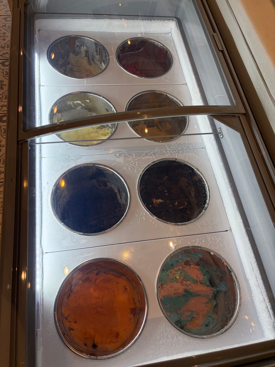 A freezer display case with eight round containers of various ice cream flavors.