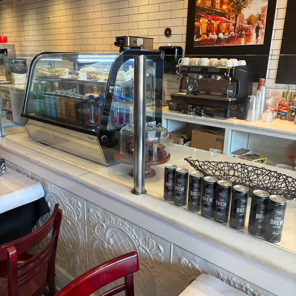 A cafe counter with a pastry display case, coffee machine, and canned cold brew.
