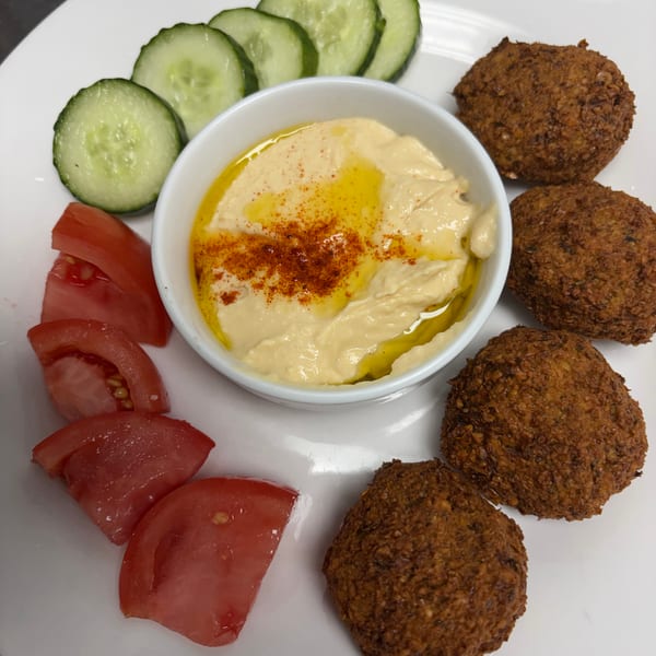 A white plate with falafel, hummus, sliced cucumbers, and tomato wedges.