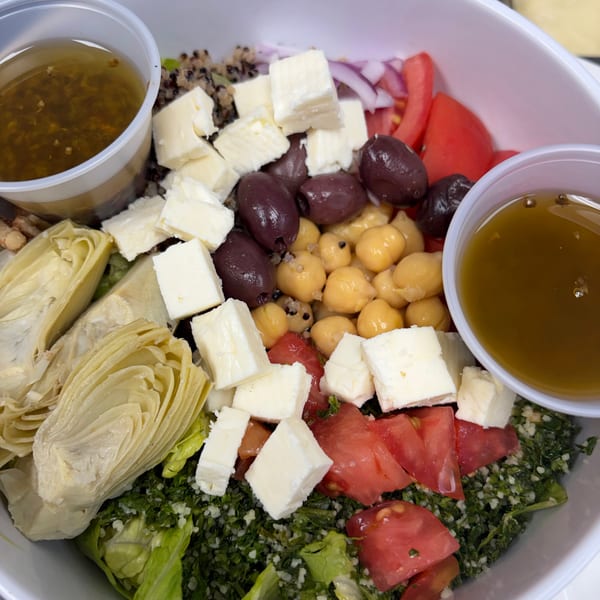 A vibrant salad with feta, olives, chickpeas, artichokes, tomatoes, and two cups of dressing.
