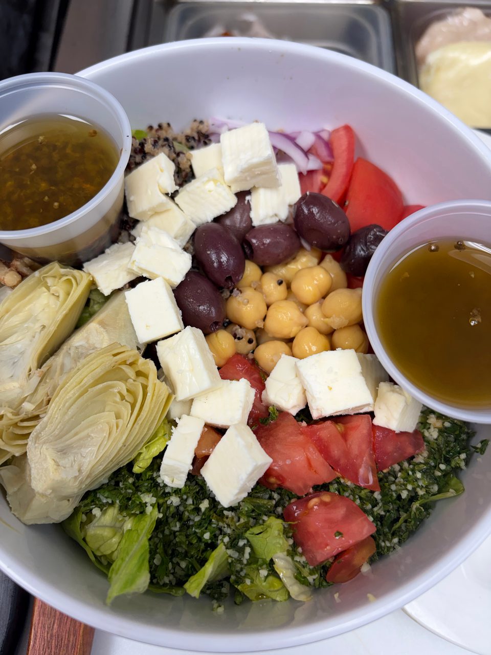 A vibrant salad with feta, olives, chickpeas, artichokes, tomatoes, and two cups of dressing.