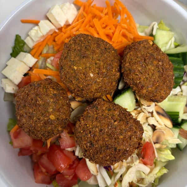 A vibrant falafel salad in a white bowl, featuring four crispy falafel, fresh vegetables, and cheese.