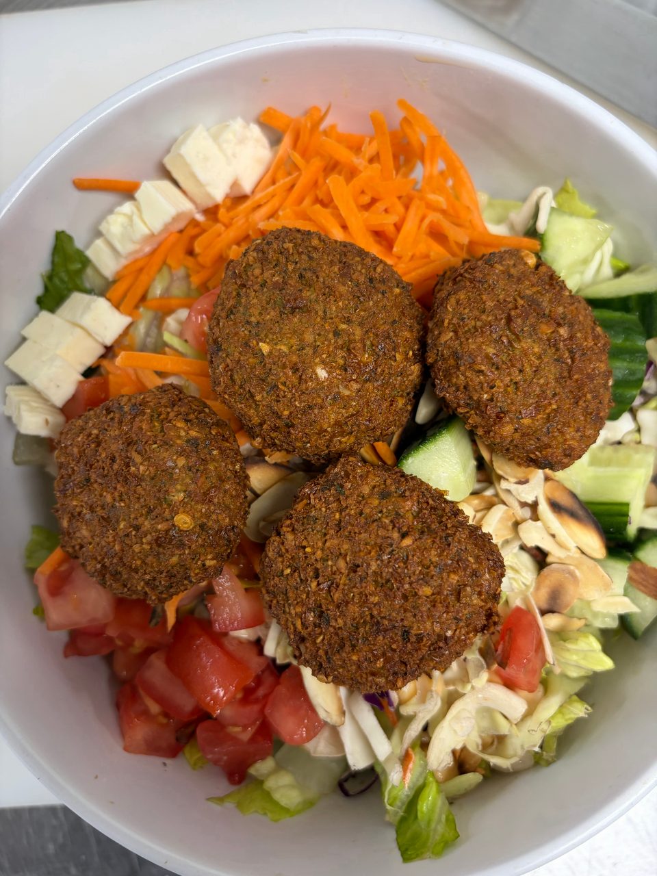 A vibrant falafel salad in a white bowl, featuring four crispy falafel, fresh vegetables, and cheese.