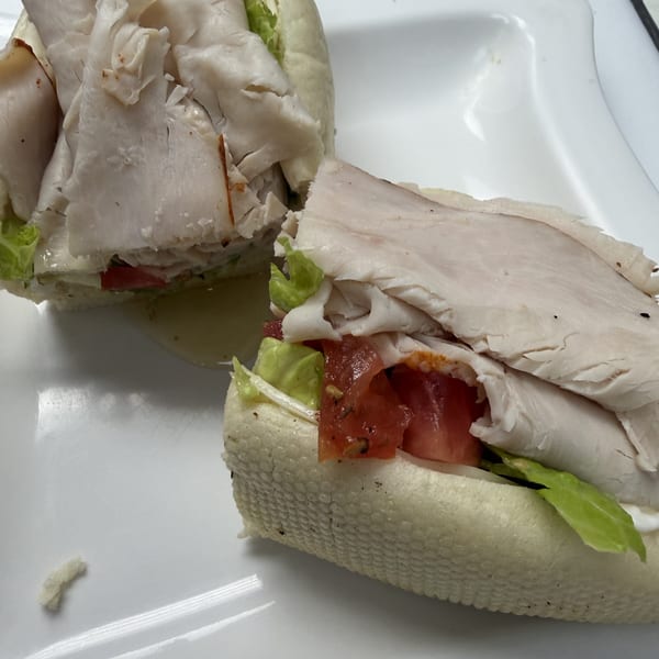 Two halves of a turkey sub sandwich with lettuce, tomato, and sauce on a white plate.