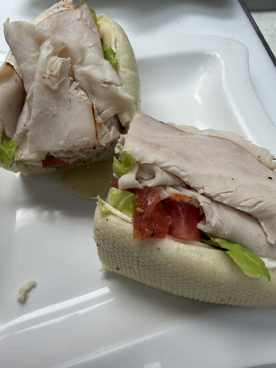 Two halves of a turkey sub sandwich with lettuce, tomato, and sauce on a white plate.